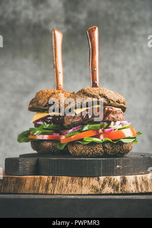 Le carni bovine cheeseburger con salsa barbecue su rustiche tavole di legno, grigio muro di cemento a sfondo, close-up, composizione verticale. Comfort food, b Foto Stock