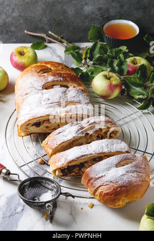 In casa fette di pasta sfoglia strudel di mele torta sulla griglia di raffreddamento servita con mature mele fresche, rami, cieve e zucchero in polvere sul marmo bianco textur Foto Stock