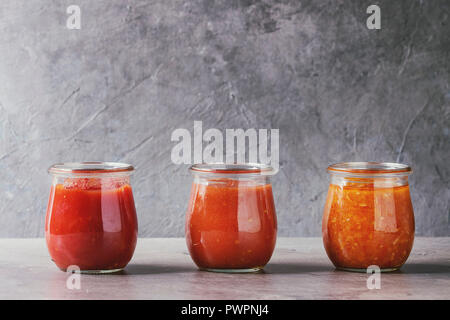 Varietà di tre fatti in casa salse di pomodoro in vasetti di vetro grigio sul tavolo da cucina. Close up Foto Stock