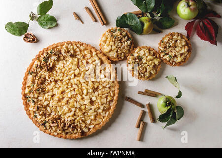 Dolci caserecci frollini apple tart e canapes con bastoncini di cannella, noci Mele rami sopra in marmo bianco dello sfondo. In autunno la cottura. Fl Foto Stock