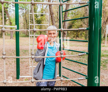 Ritratto di felice fit donna Senior con guanto di boxe in palestra esterna dell'abbigliamento sportivo. Active Anziani Lifestyle Fitness Foto Stock