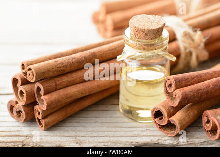 Olio di cannella e bastoncini di cannella sul pannello di legno Foto Stock