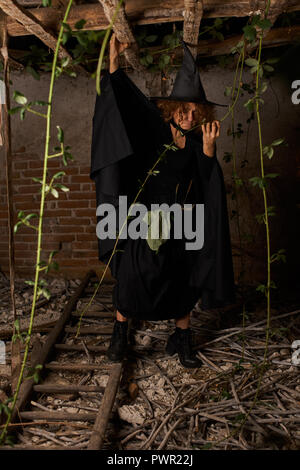 Vecchio scary strega in una casa in rovina, vestito di nero Foto Stock