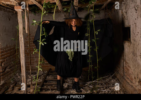 Vecchio scary strega in una casa in rovina, vestito di nero Foto Stock