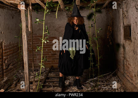 Vecchio scary strega in una casa in rovina, vestito di nero Foto Stock