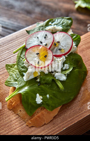 Close-up di bruschette con ravanelli, spinaci e ricotta con semi di lino su uno sfondo di legno. Foto Stock