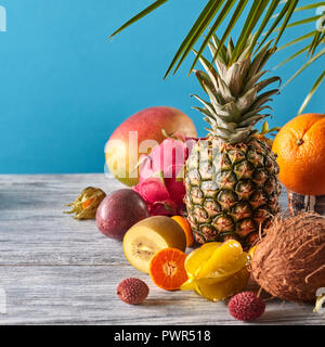 Mix esotico da frutti maturi - pineaple, dragon frutta, mango, cocco, kiwi, carambole, litchi sul grigio di un tavolo di legno su un blu. Foto Stock