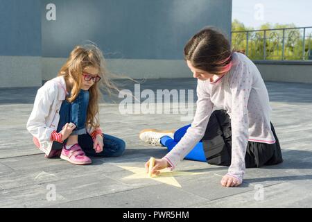 I bambini e le bambine disegnare sull'asfalto matite colorate simbolo - star. Foto Stock