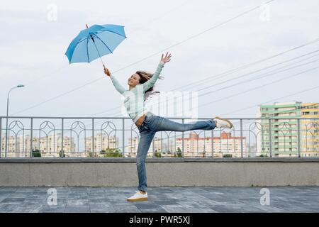 Bambina corre dietro un ombrello contro lo sfondo della città Foto Stock