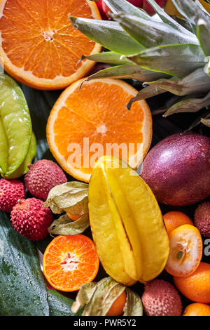 Close-up sfondo esotico con sani succosa frutta tropicale - carambole, due metà di arancia, frutto della passione, litci, ananas sulla foglia verde. Foto Stock