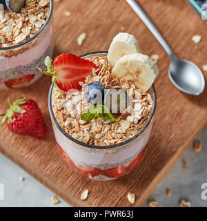 Il vetro con fiocchi di avena, frutta banane, fragole, frullato fresco, chia semi su una tavola di legno. Foto Stock