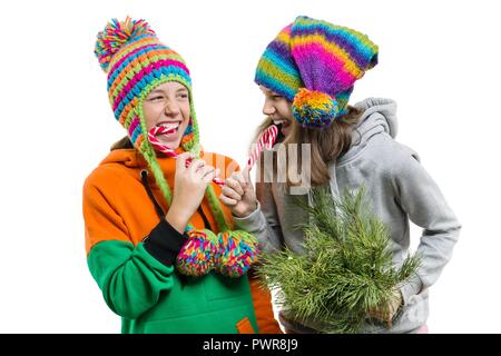 Allegro giovani ragazze adolescenti divertendosi con Natale candy canes, in inverno i cappucci a maglia, isolato su sfondo bianco. Foto Stock