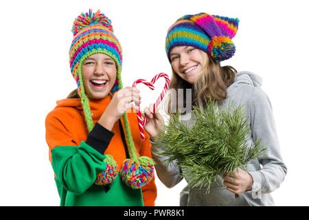 Allegro giovani ragazze adolescenti divertendosi con Natale candy canes, in inverno i cappucci a maglia, isolato su sfondo bianco. Foto Stock