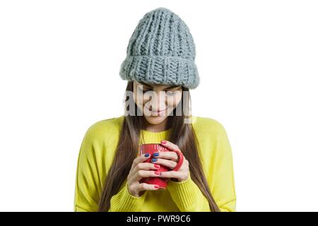 Ritratto di ragazza in Felpa gialla e cappuccio a maglia con la coppa in mano, donna cercando in tazza, sfondo bianco isolato. Foto Stock