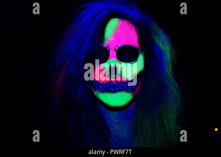 Donna con il suo volto dipinto con neon di make-up con un teschio design per Halloween Foto Stock