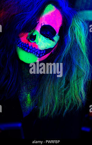 Donna con il suo volto dipinto con neon di make-up con un teschio design per Halloween Foto Stock