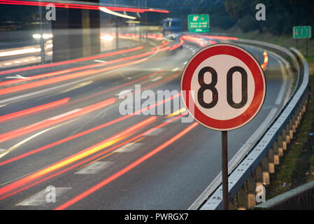 Una lunga esposizione colpo di segno di traffico che mostra 80 km/h il limite massimo di velocità su una strada piena di automobili in motion blur durante la notte Foto Stock