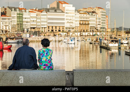 La Coruña, Spagna - Luglio 13th, 2018: una coppia matura intorno 60 anni sono seduti cercando la vista dal porto nel pomeriggio. Foto Stock