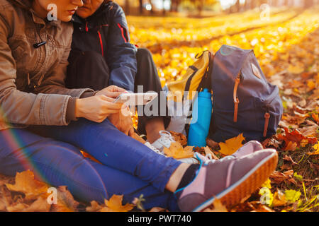 Coppia di turisti con zaini ricerca per il modo giusto usando il navigatore sul telefono nella foresta di autunno. Le donne aventi il resto Foto Stock