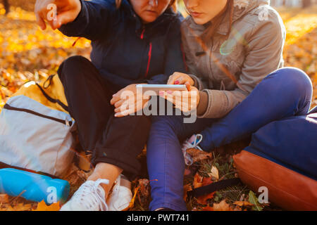 Coppia di turisti con zaini ricerca per il modo giusto usando il navigatore sul telefono nella foresta di autunno. Le donne aventi il resto Foto Stock