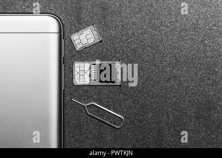 Telefono cellulare e slot aperti per nano SIM card SD micro drive e chiave di metallo su sfondo grigio con copia spazio, foto in bianco e nero Foto Stock