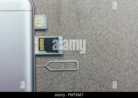 Telefono cellulare e slot aperti per nano SIM card SD micro drive e chiave di metallo su uno sfondo grigio con spazio di copia Foto Stock