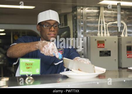 Oceano Pacifico (20 giugno 2017) specialista culinaria di terza classe Mario Murray, da Augusta, Georgia serve il pranzo nel quadrato di poppa a bordo del Wasp-classe assalto anfibio nave USS Essex (LHD 2). Essex sta conducendo un ponte di volo certificazioni e prove in mare al largo della costa della California del Sud. Foto Stock