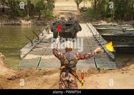 Un soldato ungherese guide Troopers assegnato al primo squadrone, 2d reggimento di cavalleria, U.S. Esercito come essi guidano i loro Stryker veicolo da combattimento su un PMP galleggiante ponte per attraversare il fiume Mosoni-Duna a Gyor, Ungheria durante l'esercizio Szentes Ax 17 Luglio 4, 2017. Il ponte è stato eruttato dagli ingegneri di 37th Engineer reggimento ungherese forza di difesa e di brigata 837th Engineer battaglione, U.S. Esercito Nazionale Guardia da Wooster, Ohio. La nazionale ungherese di esercizio avviene 26 Giugno-luglio 7 per consentire al custode di Saber 17 effettuando il bridging tattico e la acque che attraversano le operazioni per 2CR libertà di movem Foto Stock