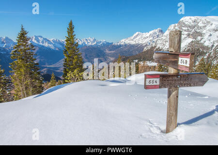 Segnavia, il cartello che indica la via verso i molti sentieri del sud delle Alpi italiane. Escursioni con le racchette da neve, le tracce sulla neve, giorno senza nuvole. Foto Stock