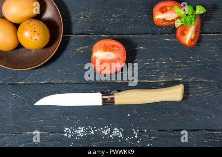 Affettare i pomodori con un coltello da tasca. Lay piatto. Sfondo scuro. Foto Stock