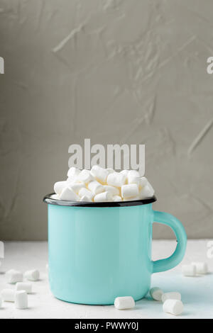 Metallo blu tazza di cacao o cioccolata calda con marshmallows sul tavolo su sfondo grigio Foto Stock