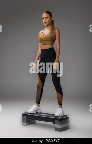 Attraente giovane donna facendo step aerobics su grigio Foto Stock