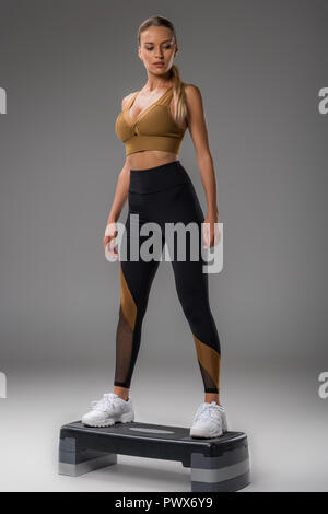 Montare la giovane donna facendo step aerobics su grigio Foto Stock