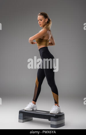 Atletica Giovane donna facendo step aerobics su grigio Foto Stock