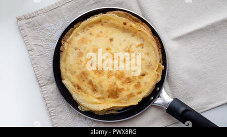 Pila di Slavic nazionale sottili frittelle dorate in padella con asciugamano rustico di campagna stile; minimalismo, sfondo bianco; piatto tradizionale 'bliny" Foto Stock