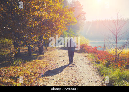 Un uomo cammina lungo un percorso in un parco nei pressi di un lago al mattino presto in autunno Foto Stock