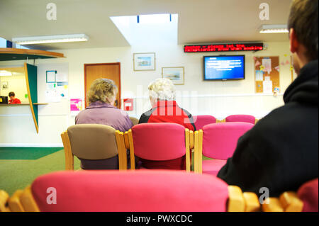 Anziani malati a sedersi in un GP chirurgia sala di attesa, in attesa di essere visto dal medico o da un infermiere Foto Stock