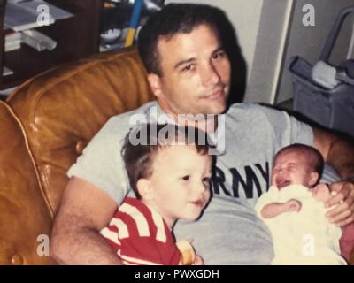 Tom Rayburn, un ora-pensionati U.S. Esercito difesa aerea e ispettore generale officer, mantiene i suoi figli, 3-anno-vecchia Scott e Kaitlin infantile nella famiglia, la casa di Fort Bliss, Texas, nel 1989. Scott e Kaitlin, ora entrambi i comandanti dell'esercito, recentemente riunificata in Occidente Qayyarah Airfield, Iraq, come Kaitlin guardato il suo fratello prendere il comando per la prima volta. Foto Stock