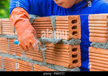 Femmina di lavoratore edile che stabilisce un muro di mattoni uno per uno tramite mortaio per collegare e sigillare gli spazi tra di essi Foto Stock