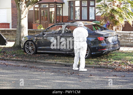 Liverpool, Regno Unito. Il 18 ottobre 2018. Un cordone di polizia attorno ad un bruciato auto in strada Abbeystead Childwall. Un colore scuro Audi abbandonate su un orlo di erba, 1.7 miglia da ultima notte di riprese in Alderson Rd, Wavertree. Un forensics officer è di scattare foto e la raccolta delle prove sulla scena. La polizia non sono dicendo in questa fase se la vettura è stata coinvolta in ultima notte di omicidio. Credito: Ken Biggs/Alamy Live News. Foto Stock