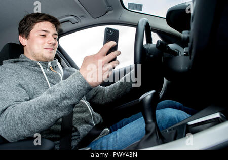 Laatzen, Germania. Xviii oct, 2018. Un giovane uomo è seduto alla pratica area dell'ADAC guida centro di sicurezza con uno smartphone in mano al volante di un'auto. Durante il viaggio, deve essere dimostrato che l'uso di un semaforo app previsto dalla città di Hannover potrebbe essere associato con un elevato rischio di incidenti. ADAC, FDP, Camera dei mestieri e le associazioni imprenditoriali (UVN) opporsi all'introduzione dell'App. Credito: Hauke-Christian Dittrich/dpa/Alamy Live News Foto Stock