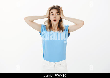 Oh non posso crederci. Ritratto di colpito e stordito affascinante unione studentessa in blu t-shirt, tenendo la testa con le palme, la caduta di ganascia e fissando la telecamera dalla sorpresa e divertimento Foto Stock