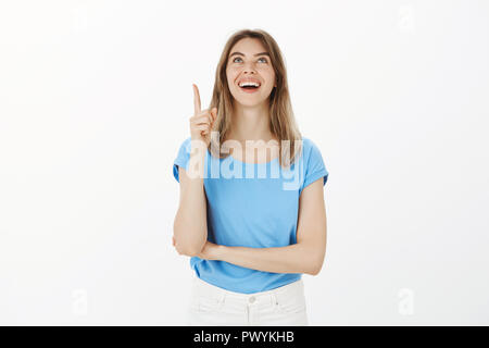 Ragazza in piedi sulla strada vedendo amico sul balcone. Ritratto di felice giovane positivo e femminile donna con capelli biondi, puntamento e guardando con sorriso luminoso, essendo interessato con la cosa divertente Foto Stock