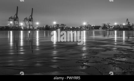 Vista panoramica sul fiume e la porta con il cargo cranes, contenitori, i proiettori su una sera d'inverno. Lunga esposizione. In bianco e nero. Foto Stock