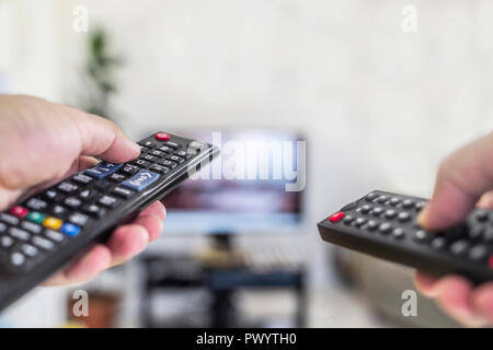 Guardare la tv e utilizzando due telecomando Foto Stock