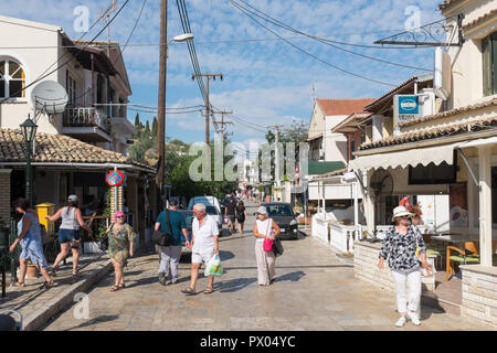 I turisti a piedi lungo la strada principale che corre attraverso la bella Corfù villaggio costiero di Kassiopi Foto Stock