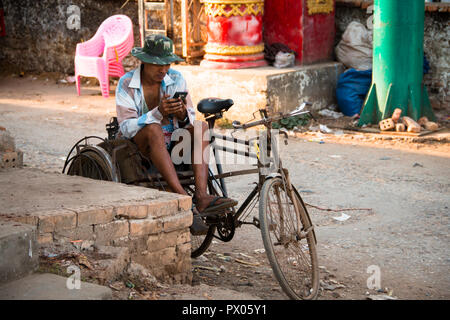 Di Hpa-an, MYANMAR - Marzo 2018: un uomo e il suo telefono cellulare seduto su una vecchia bicicletta nel centro di Hpa-An in Myanmar Foto Stock