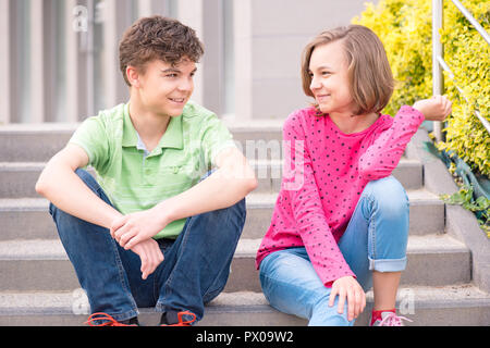 Felice ragazzo adolescente e ragazza sorridente all'esterno. Giovane sorella e fratello teens seduta sulle scale e guardare a ogni altro. Foto Stock