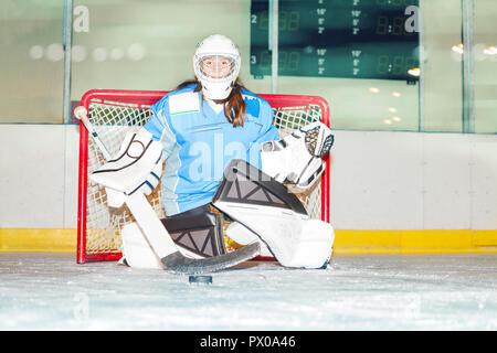 Goaltender femmina si accovaccia nella piega per proteggere la rete contro puck Foto Stock