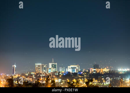 Un ampio panorama di Kigali skyline della città illuminata di notte, al di sotto di un profondo blu del cielo della sera Foto Stock